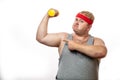 Fat funny man in red headband shows his muscles with dummbell and emotions Royalty Free Stock Photo