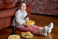 Fat girl eating chips from bowl while sitting on floor in living room, side view Royalty Free Stock Photo