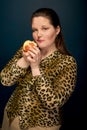 A fat girl holds a red apple near her face and looks at the camera. Dark blue background. Royalty Free Stock Photo