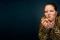 Fat girl in a leopard blouse with a hamburger in her hand. Empty space on the left. Bright makeup.