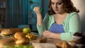 Fat lady exercising with dumbbell and looking at sweet donut, dieting willpower Royalty Free Stock Photo