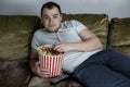 Fat lazy man lying on the couch watching TV and eating popcorn Royalty Free Stock Photo