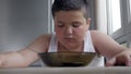 Fat little boy in white t-shirt sits at table looks in empty plate. thoughts and concentration.