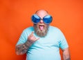 Fat man with beard, tattoos and sunglasses makes the gesture of the horns