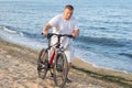 A fat man drives a bicycle along the seashore during the day