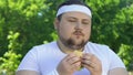 Fat man eating burger after workout, addicted to junk food, lack of willpower