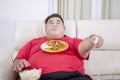 Fat man grabbing popcorns while holding tv remote Royalty Free Stock Photo