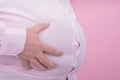 Fat man hand holding his big belly on a pink background: typical photo for beer belly: Selective focus