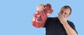 Fat man is holding a raw piece of meat. person covers his mouth with his hand. vegetarian should not eat meat products. abstinence Royalty Free Stock Photo