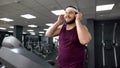 Fat man putting on headset and listening to music during jogging on treadmill Royalty Free Stock Photo