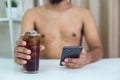 Fat man shirtless holding black sweet drink glass use your smartphone. Male drink sugar calorie. Dieting healthy concept, lose