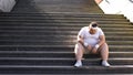 Fat man sitting on stairs after jogging, no faith in himself, insecurities Royalty Free Stock Photo