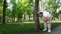 Fat man tired after running in park, leaning on tree, tiresome workouts outdoors Royalty Free Stock Photo