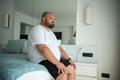 Fat guy sitting on bed with disgruntled face. Guy woke up from heat stuffiness high temperature Royalty Free Stock Photo