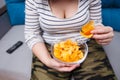 Fat overweight woman sitting on the sofa, eating chips while wat Royalty Free Stock Photo