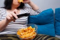 Fat overweight woman sitting on the sofa, eating chips while wat Royalty Free Stock Photo