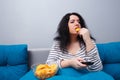 Fat overweight woman sitting on the sofa, eating chips while wat Royalty Free Stock Photo