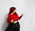 Obese ginger lady in red spiked top, black bra and leather skirt. She is dancing, posing isolated on white photo background