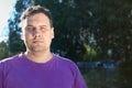 Fat serious man in t-shirt poses outdoor in sunlight