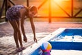 A girl with hair braided in a bun in bright suit plays by the pool with a ball against the background of summer sun Royalty Free Stock Photo