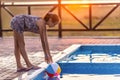 A girl with hair braided in a bun in bright suit plays by the pool with a ball against the background of summer sun Royalty Free Stock Photo