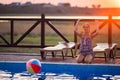 A girl with hair braided in a bun in bright suit plays by the pool with a ball against the background of summer sun Royalty Free Stock Photo