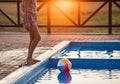 A girl with hair braided in a bun in bright suit plays by the pool with a ball against the background of summer sun Royalty Free Stock Photo