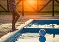 A girl with hair braided in a bun in bright suit plays by the pool with a ball against the background of summer sun Royalty Free Stock Photo