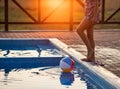 A girl with hair braided in a bun in bright suit plays by the pool with a ball against the background of summer sun Royalty Free Stock Photo