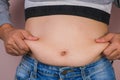 Fat woman hand holding excessive belly fat  on pink background. Overweight fatty belly of woman. Female diet and body Royalty Free Stock Photo