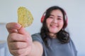 Fat woman holding potato chips indoors while listening music