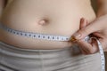 A fat woman measures her waist with a measuring tape, close-up. Lifestyle, diet concept. Royalty Free Stock Photo