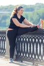 fat woman performs exercises on the embankment in the city park