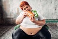 Fat woman sits in chair and eats sandwich, bulimic