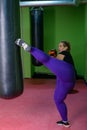 A fat woman is trying to lose weight doing kickboxing. A girl in boxing gloves kicks a punching bag. Royalty Free Stock Photo