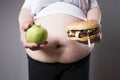 Fat women suffer from obesity with big hamburger and apple in hands, junk food concept