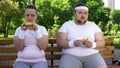 Fat young couple eating hamburgers, addicted to junk food, lack of willpower