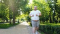 Fat young man jogging in park, obesity concept, struggling with insecurity