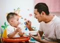 Father acting Mom feeding his son baby 1 year old on chair Royalty Free Stock Photo