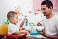 Father acting Mom feeding his son baby 1 year old on chair Royalty Free Stock Photo