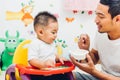 Father acting Mom feeding his son baby 1 year old on chair Royalty Free Stock Photo