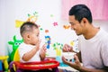 Father acting Mom feeding his son baby 1 year old on chair Royalty Free Stock Photo