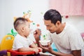 Father acting Mom feeding his son baby 1 year old on chair Royalty Free Stock Photo