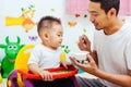 Father acting Mom feeding his son baby 1 year old on chair Royalty Free Stock Photo