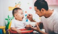 Father acting Mom feeding his son baby 1 year old on chair Royalty Free Stock Photo