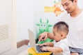 Father acting Mom feeding milk his son baby 1 year old while working on laptop computer Royalty Free Stock Photo