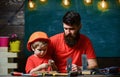 Father as handyman concept. Father, parent with beard and little son in classroom, chalkboard on background. Boy, child
