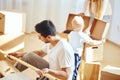 Father assembling furniture in living room of new apartment, mother with son and pile of moving boxes on background