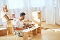 Father assembling furniture in living room of new apartment, mother with son and pile of moving boxes on background Royalty Free Stock Photo