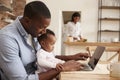 Father And Baby Daughter Use Laptop As Mother Prepares Meal Royalty Free Stock Photo